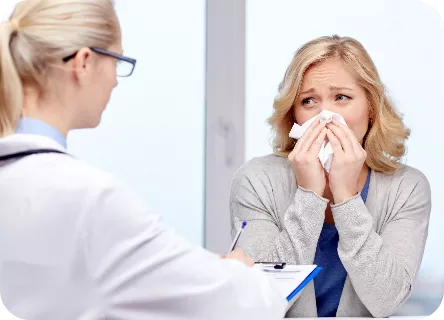 Ärztin berät eine niesende Patientin zur Behandlung der allergischen Rhinitis
